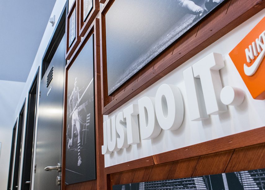 Close-up van een Nike-winkelbord met de slogan 'Just Do It' in grote witte letters, naast het oranje Nike-logo op een houten achtergrond
