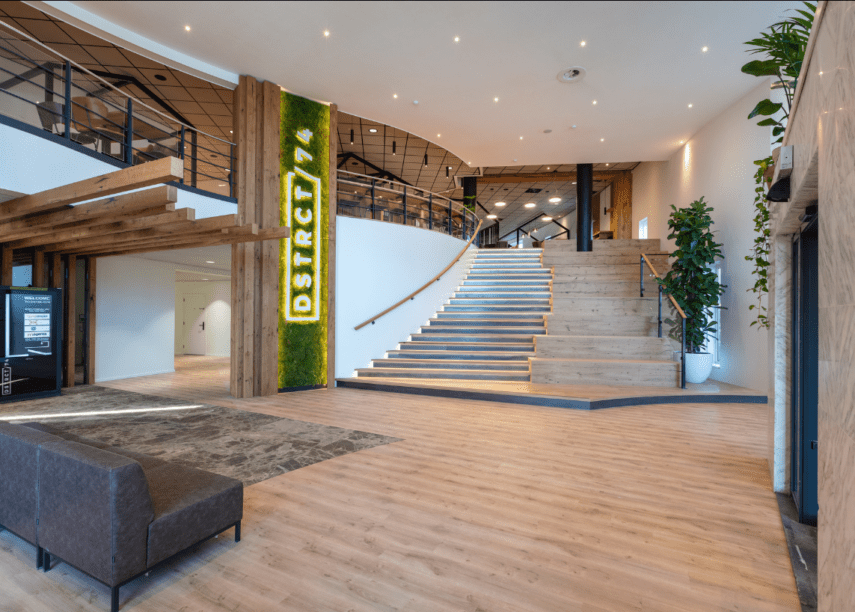 De entree van een kantoorpand met lichte en groene kleuren met de naam DSTRCT/74